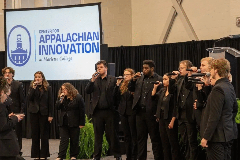 Marietta College Unveils Appalachian Innovation Center for Ohio Growth A student choir performs on stage in front of a large projection screen displaying the logo for the Center for Appalachian Innovation at Marietta College.